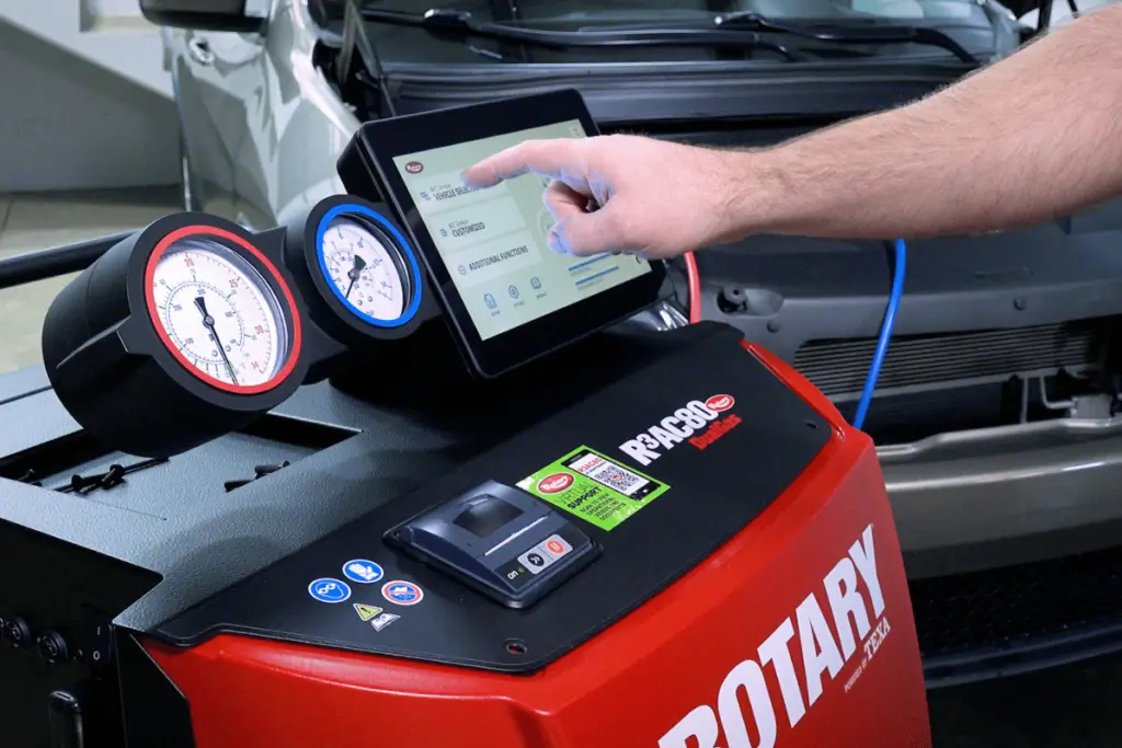 Rotary A/C recovery machines with digital interface and pressure gauges in an automotive repair shop.
